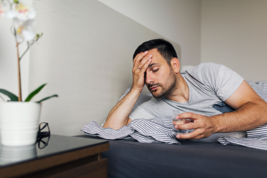 man in bed holding his head in need of a migraine chiropractor